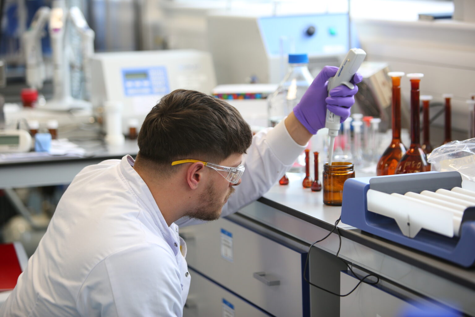 Man with brown hair in lab coat crouches beside lab bench pipetting sample for OINDP development services.