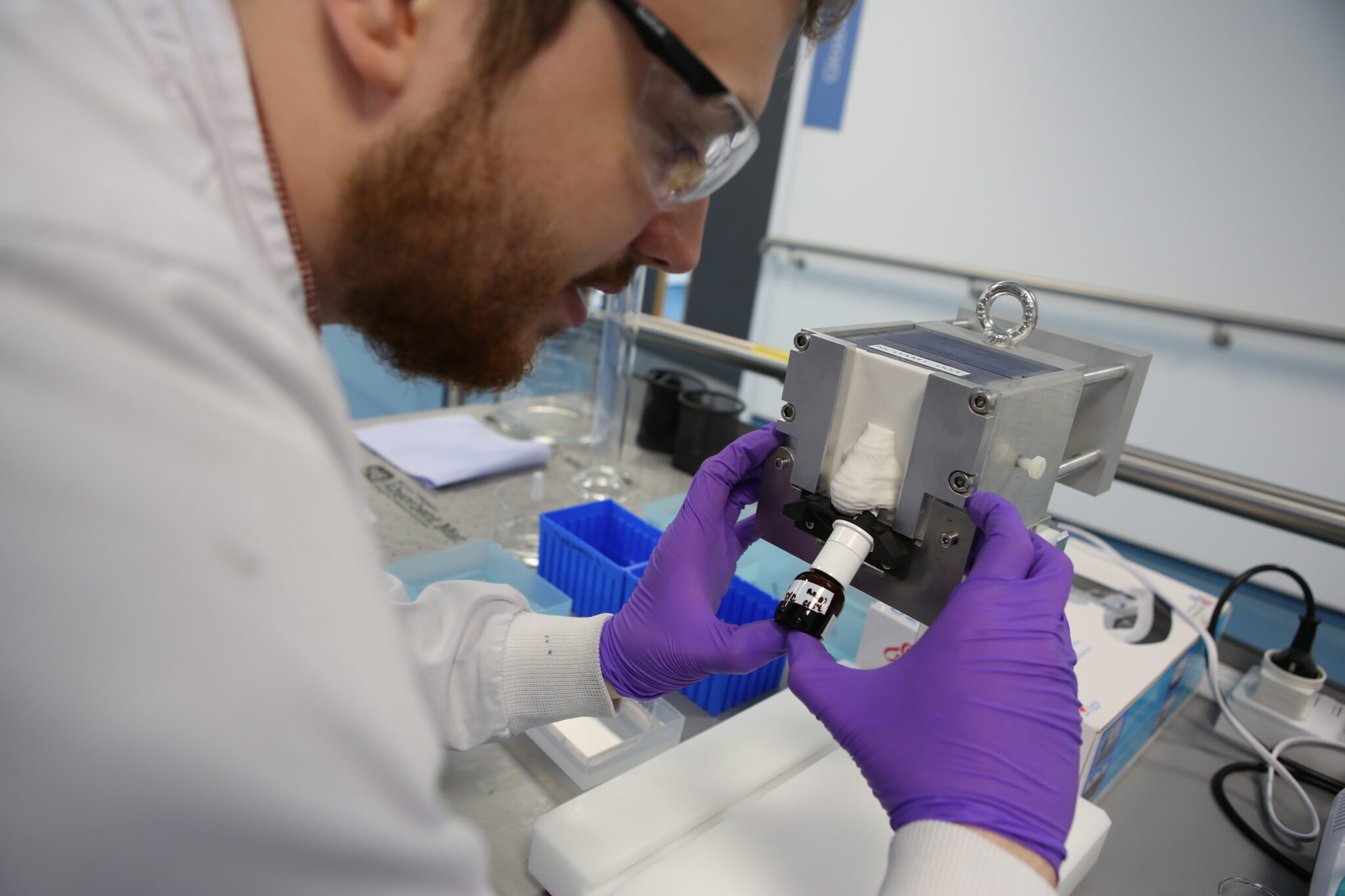 Bearded and gloved scientist in white lab coat administers nasal spray to Nanopharm's Nasal CAST in-vitro deposition model.