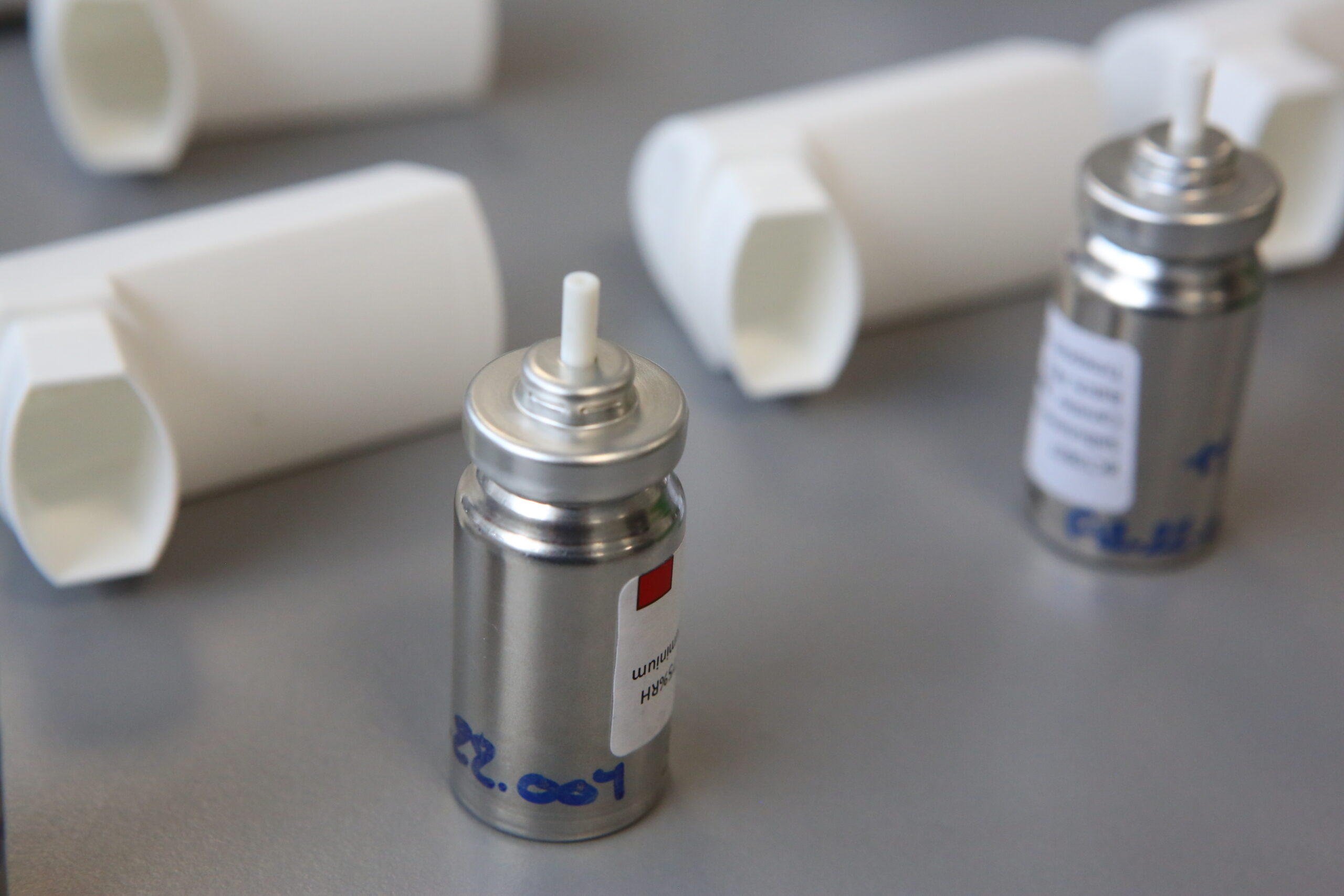 Two shiny metal pMDI inhaler cannisters on table with development codes beside white inhaler shell at Nanopharm