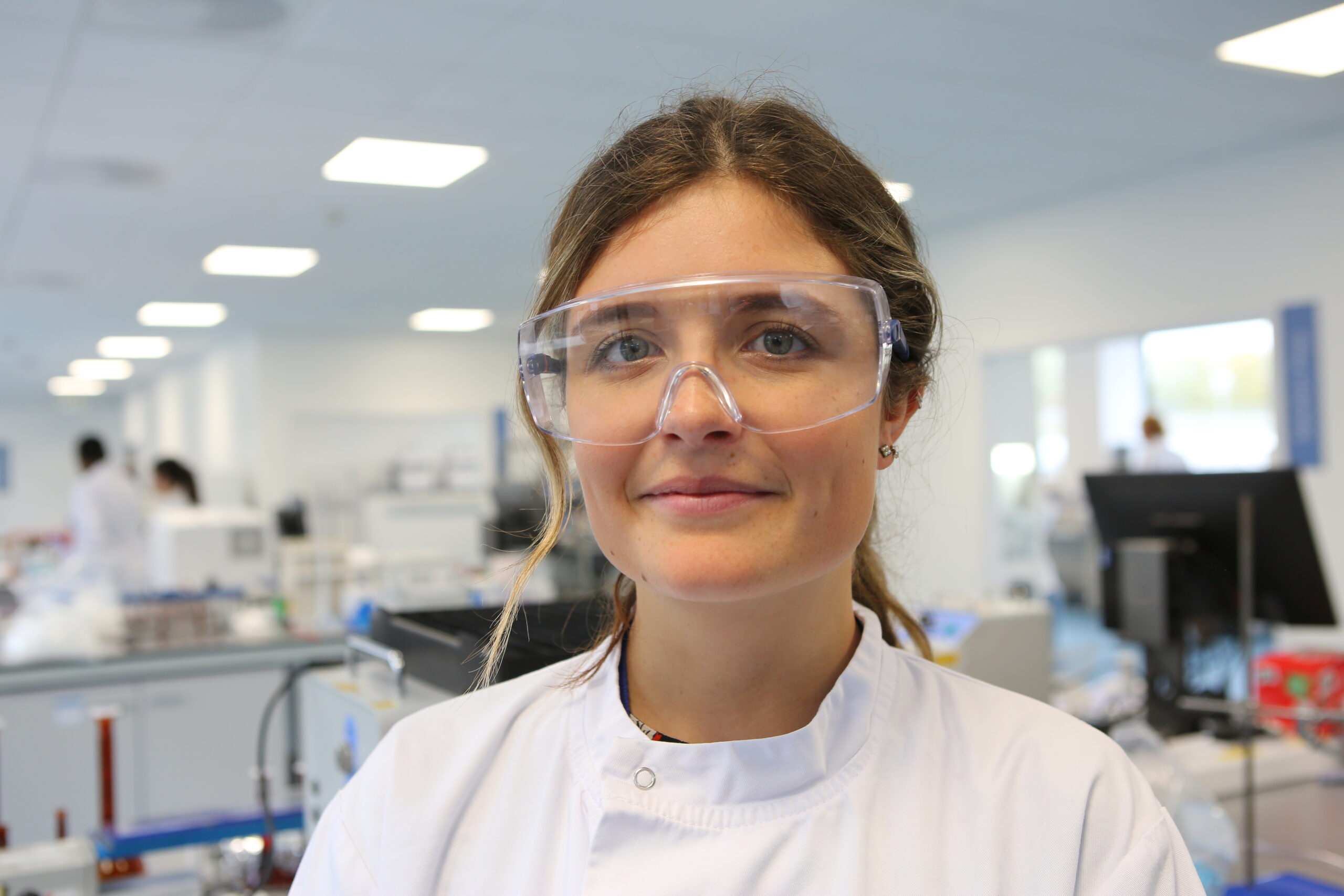 Nanopharm woman scientist wearing buttoned lab coat and safety glasses standing in cGMP laboratory lab for OINDPs.