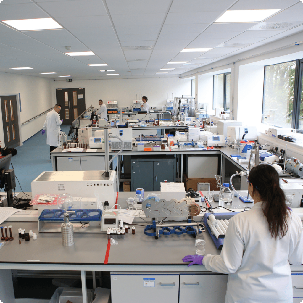 Five Nanopharm scientists in white lab coats working in cGMP laboratory with 4 benches of analytical apparatus.