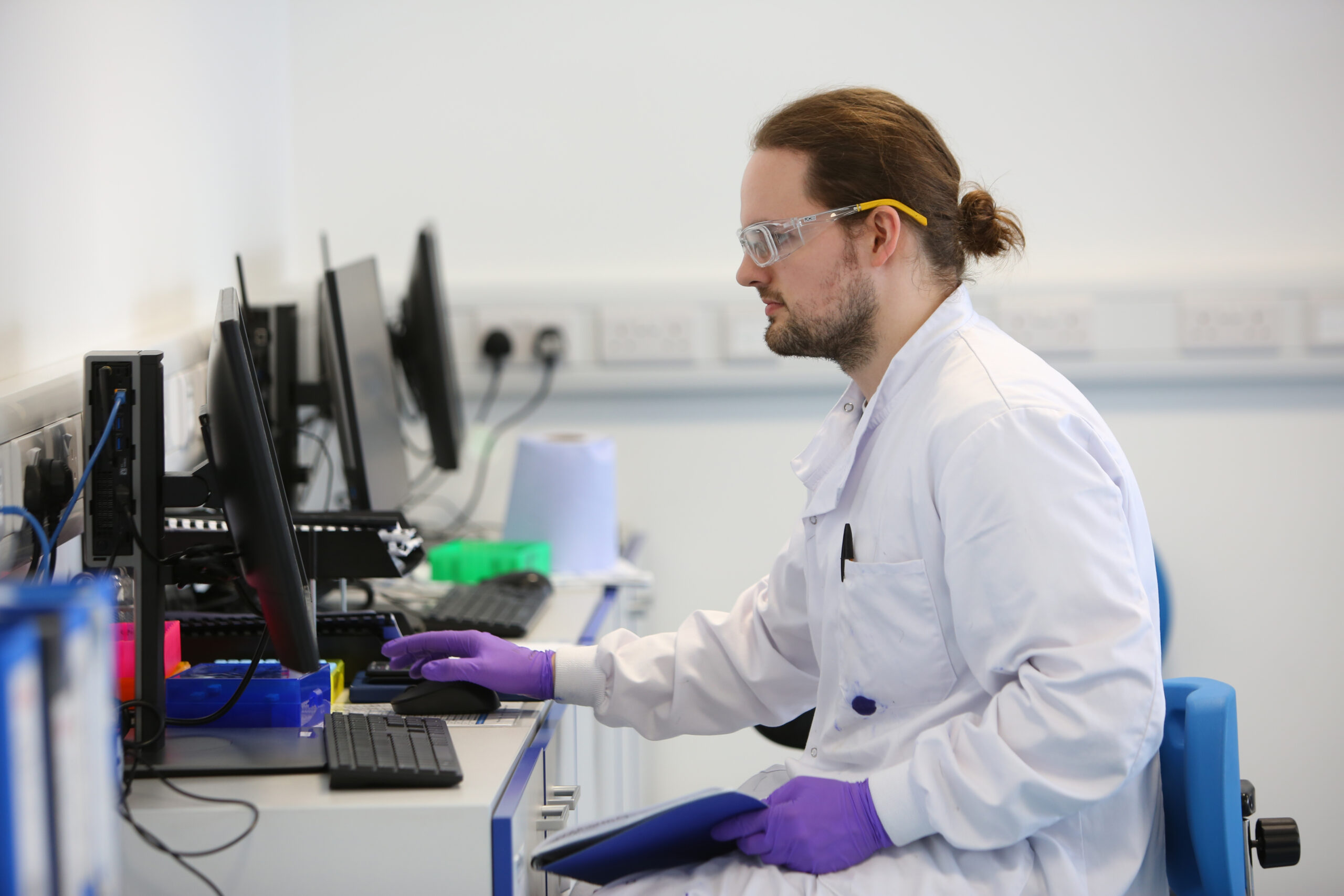 Nanopharm bearded scientist with long hair in a lab coat reviews OINDP development data on computer screen.