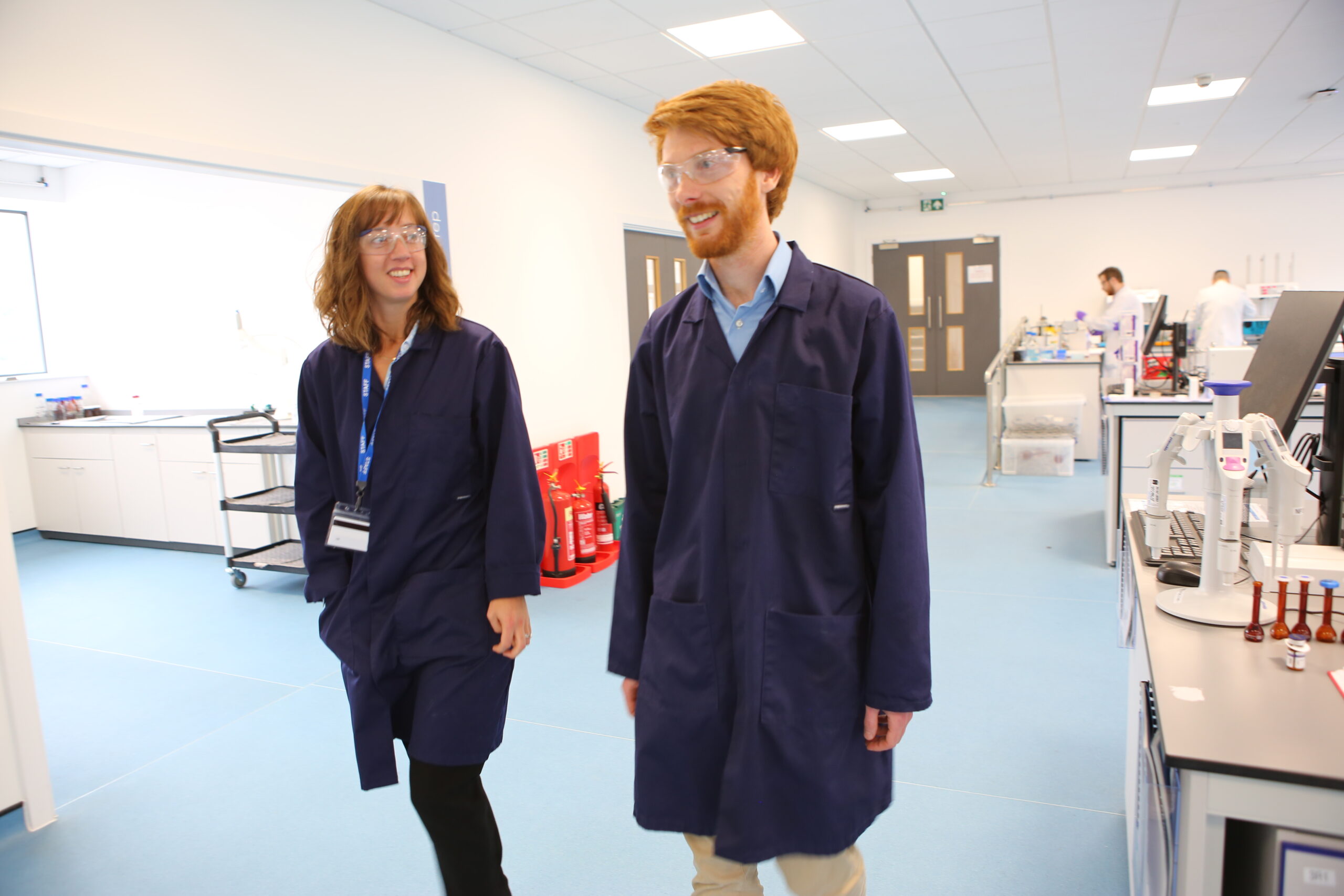 Two scientists in blue lab coats walk through a development lab at Nanopharm, dedicated to nasal and inhaled drug products.
